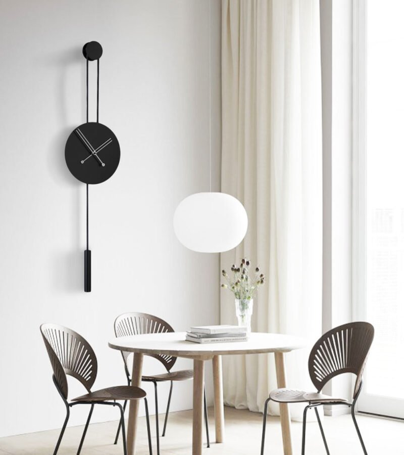 Salon için Şık Duvar Saatleri arasında olan gümüş akrep yelkovanlı siyah Halatlı Duvar Saati Avvolo 30 sandalye ve masa olan odada duvarda asılı durmakta